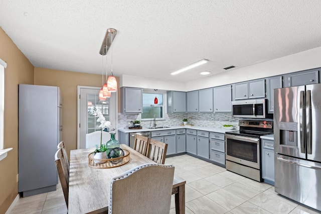 kitchen featuring sink, appliances with stainless steel finishes, gray cabinetry, hanging light fixtures, and decorative backsplash