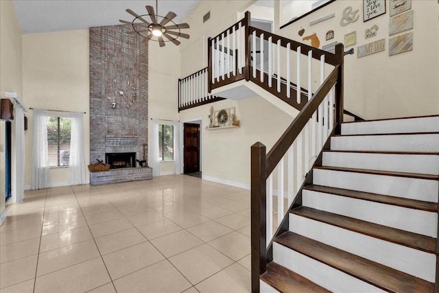 stairs featuring a fireplace, tile patterned floors, ceiling fan, and a high ceiling