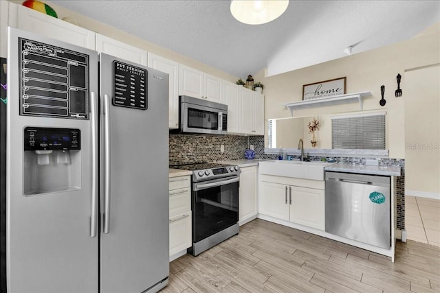 kitchen with lofted ceiling, appliances with stainless steel finishes, sink, and white cabinets