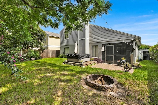 back of property featuring a patio area, a hot tub, a lawn, a fire pit, and a sunroom