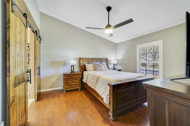 bedroom featuring lofted ceiling, ceiling fan, wood-type flooring, a textured ceiling, and a barn door