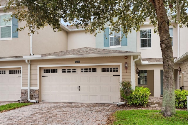 townhome / multi-family property featuring stone siding, roof with shingles, decorative driveway, and stucco siding