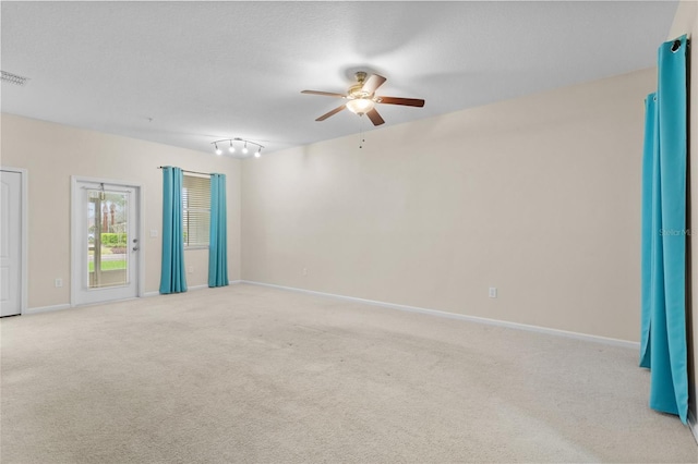 empty room featuring visible vents, light colored carpet, a ceiling fan, a textured ceiling, and baseboards