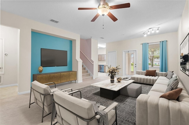 living area featuring light carpet, baseboards, visible vents, a ceiling fan, and stairway