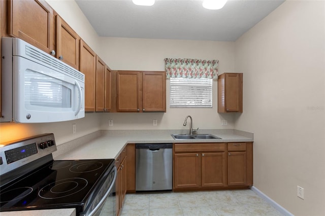 kitchen with light countertops, appliances with stainless steel finishes, a sink, and brown cabinets