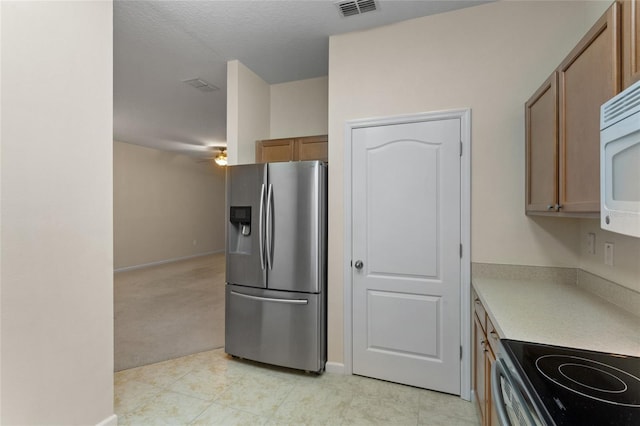 kitchen featuring brown cabinets, light countertops, visible vents, stainless steel fridge, and baseboards