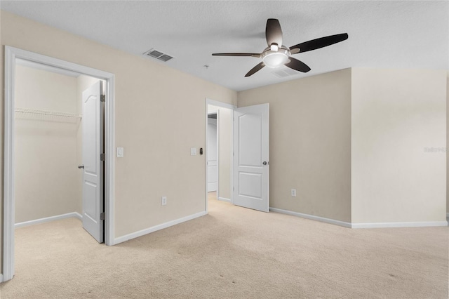 unfurnished bedroom with a walk in closet, light colored carpet, visible vents, and baseboards