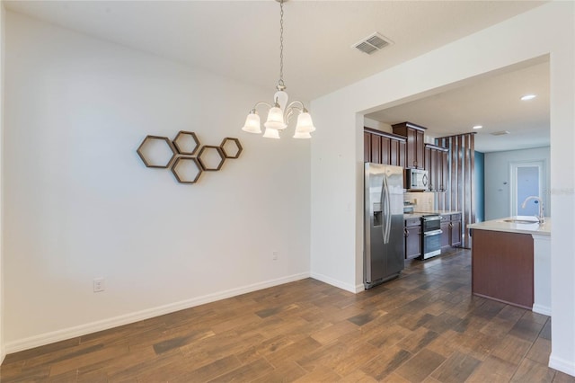 kitchen with appliances with stainless steel finishes, decorative light fixtures, sink, a notable chandelier, and dark wood-type flooring