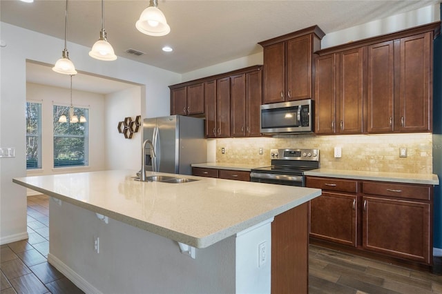 kitchen featuring decorative light fixtures, stainless steel appliances, and a center island with sink