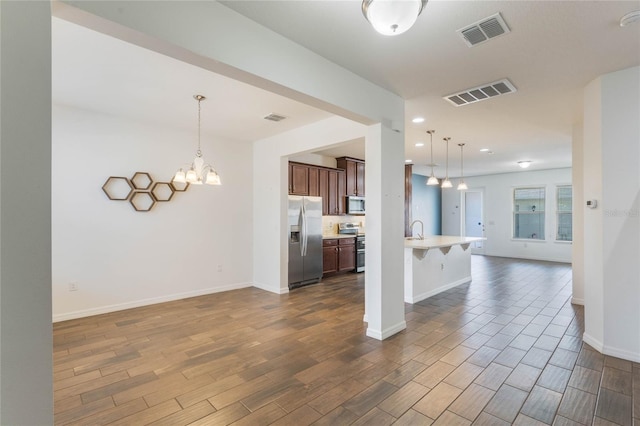 kitchen featuring a breakfast bar area, dark wood-type flooring, stainless steel appliances, a notable chandelier, and decorative light fixtures