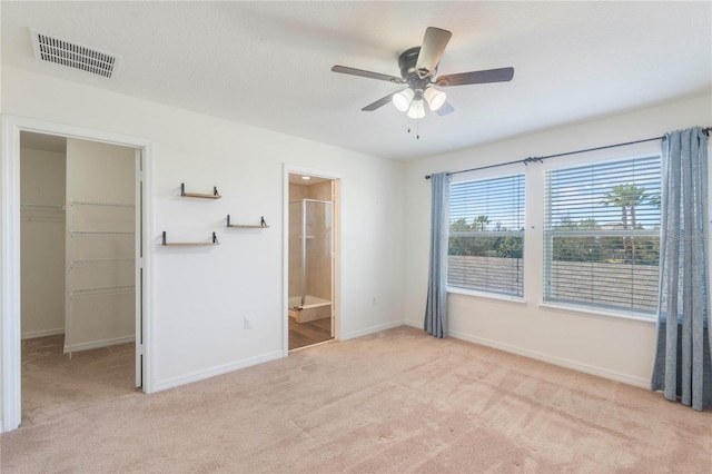 unfurnished bedroom featuring ceiling fan, a walk in closet, a closet, and light carpet