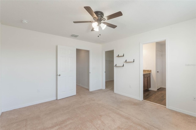 unfurnished bedroom with ensuite bathroom, a spacious closet, light colored carpet, a closet, and ceiling fan