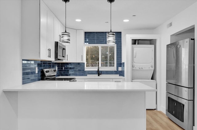 kitchen with stacked washing maching and dryer, appliances with stainless steel finishes, white cabinets, and kitchen peninsula