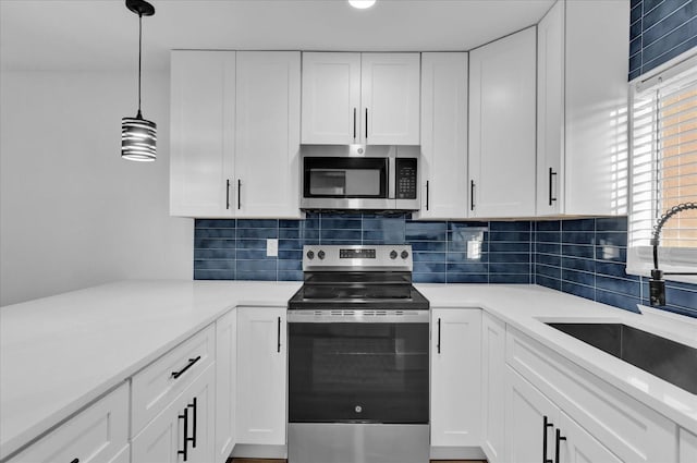 kitchen featuring sink, white cabinetry, hanging light fixtures, stainless steel appliances, and decorative backsplash