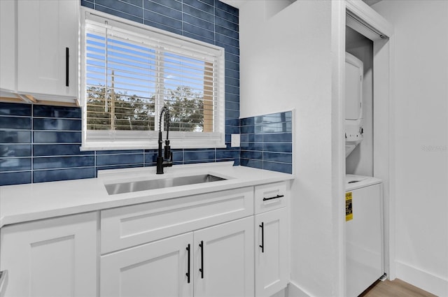 kitchen with white cabinetry, sink, light hardwood / wood-style floors, and stacked washer and clothes dryer