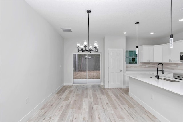 unfurnished dining area with baseboards, visible vents, light wood-type flooring, a chandelier, and a sink