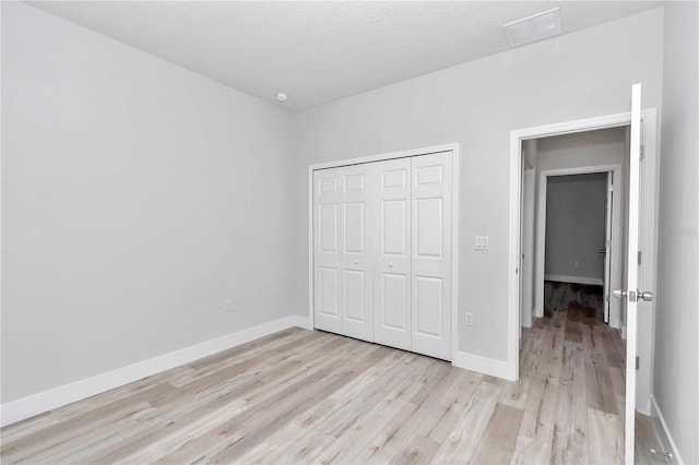 unfurnished bedroom featuring a textured ceiling, visible vents, baseboards, a closet, and light wood-type flooring