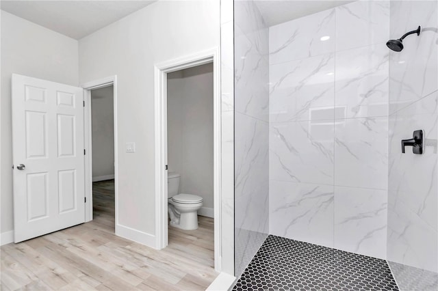 bathroom featuring baseboards, toilet, a marble finish shower, and wood finished floors