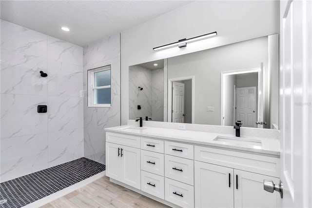 full bath with double vanity, a marble finish shower, a sink, and wood finished floors