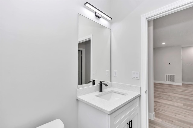 bathroom with toilet, wood finished floors, vanity, visible vents, and baseboards