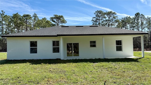 back of property featuring stucco siding, a shingled roof, and a yard