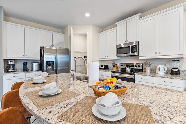 kitchen featuring white cabinetry, stainless steel appliances, a kitchen bar, and light stone countertops