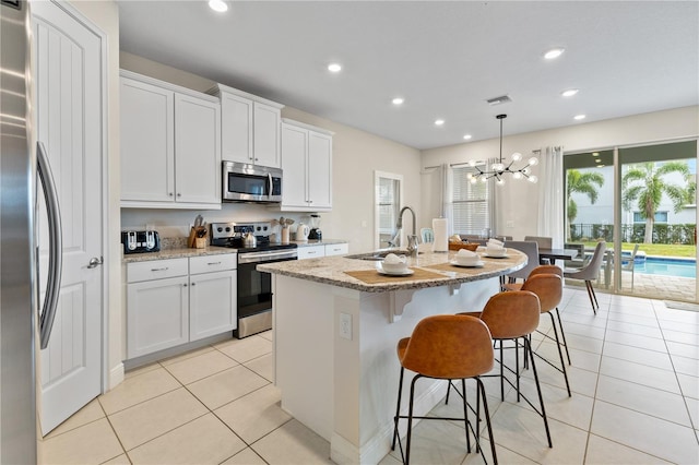 kitchen featuring decorative light fixtures, white cabinetry, sink, a kitchen island with sink, and stainless steel appliances