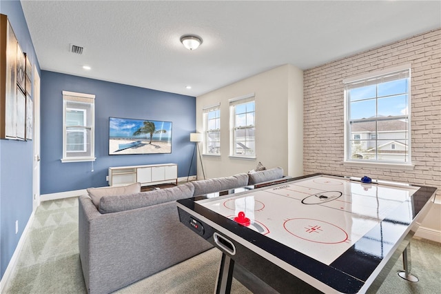 game room featuring light carpet, a textured ceiling, and brick wall