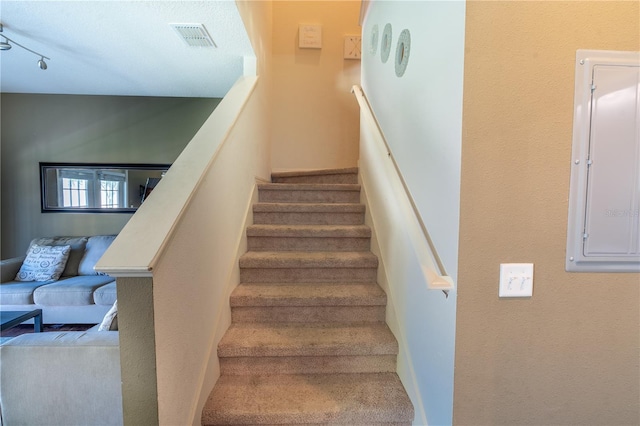 stairway with rail lighting, carpet floors, and electric panel