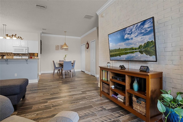 living room with dark wood-type flooring, ornamental molding, a textured ceiling, and brick wall