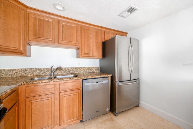 kitchen with light stone counters, sink, stainless steel appliances, and a textured ceiling