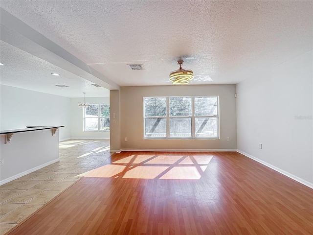 spare room featuring a chandelier, a textured ceiling, and light hardwood / wood-style flooring