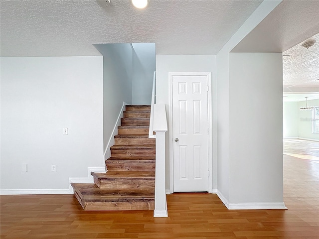 stairway with wood-type flooring, an inviting chandelier, and a textured ceiling