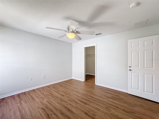 unfurnished bedroom featuring dark wood-type flooring, ceiling fan, a textured ceiling, and a walk in closet