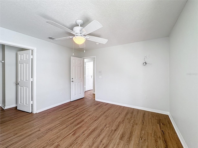 empty room with ceiling fan, wood-type flooring, and a textured ceiling