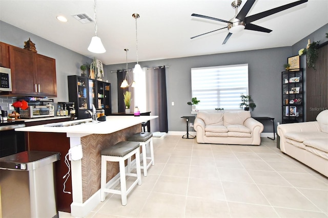 kitchen featuring light tile patterned flooring, a breakfast bar, decorative light fixtures, sink, and a center island with sink