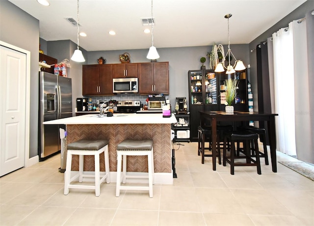 kitchen featuring tasteful backsplash, decorative light fixtures, stainless steel appliances, and an island with sink