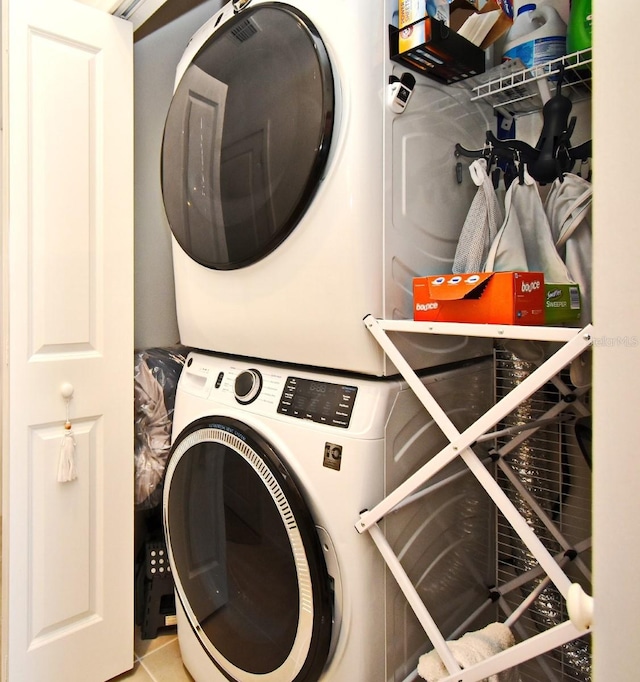 laundry room with light tile patterned flooring and stacked washer / dryer