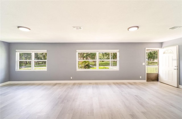 empty room with plenty of natural light, a textured ceiling, and light wood-type flooring