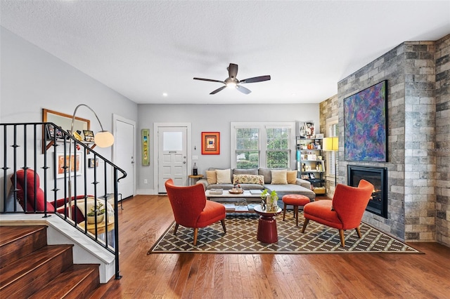 living room featuring ceiling fan, a large fireplace, hardwood / wood-style floors, and a textured ceiling