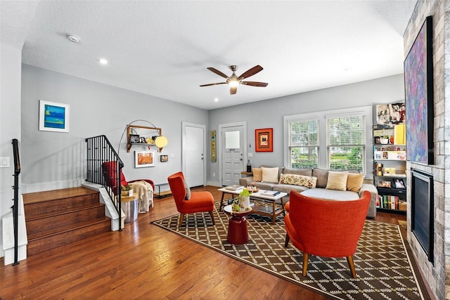 living room with hardwood / wood-style flooring, a textured ceiling, a large fireplace, and ceiling fan