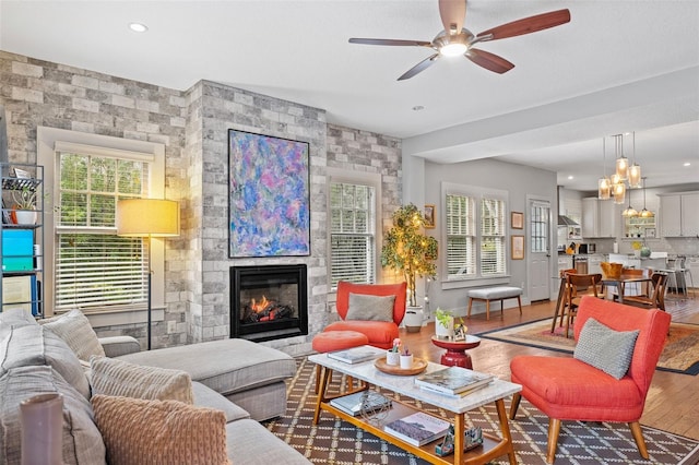 living room featuring ceiling fan, a large fireplace, and wood-type flooring