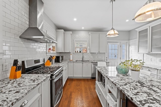 kitchen featuring wall chimney exhaust hood, sink, pendant lighting, stainless steel appliances, and white cabinets