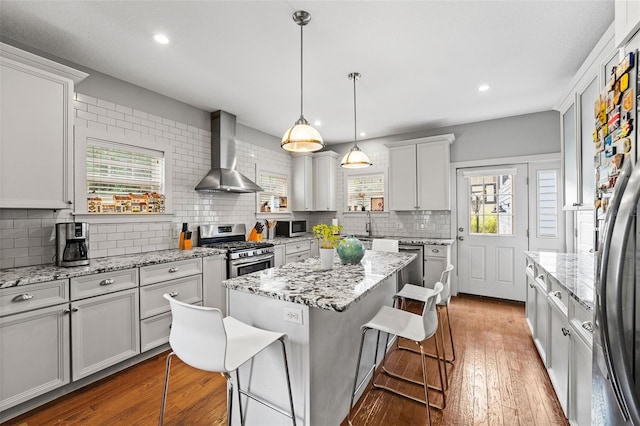 kitchen with stainless steel appliances, a kitchen island, a kitchen bar, and wall chimney exhaust hood