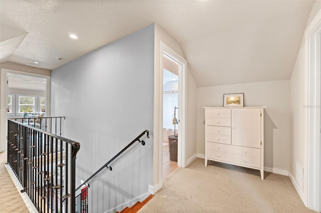 stairway with carpet flooring, vaulted ceiling, and a textured ceiling