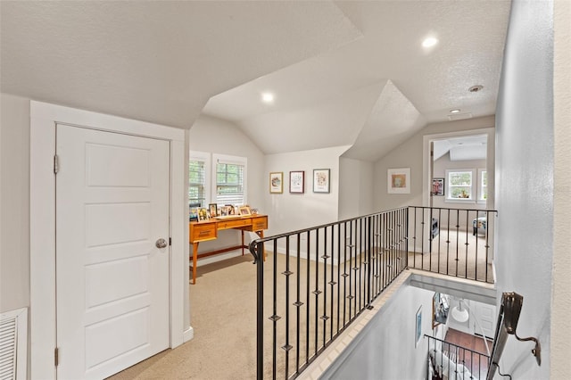 hallway with a healthy amount of sunlight, vaulted ceiling, light carpet, and a textured ceiling