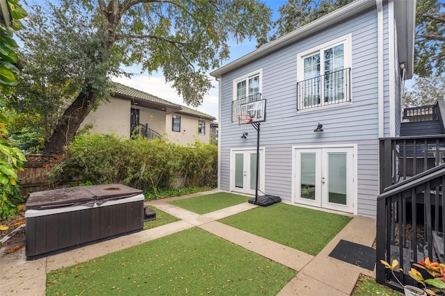 rear view of property with a lawn, a hot tub, and french doors