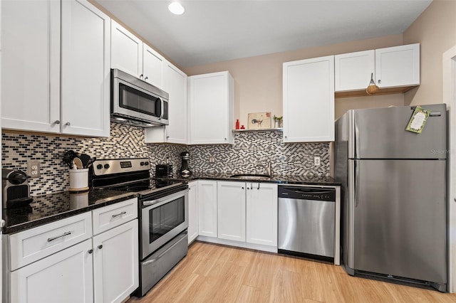 kitchen with appliances with stainless steel finishes, sink, white cabinets, dark stone counters, and light wood-type flooring