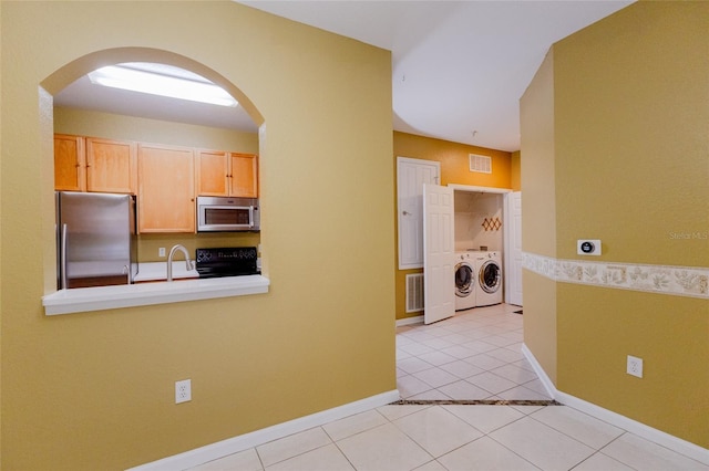 kitchen with sink, light brown cabinets, light tile patterned floors, stainless steel appliances, and washing machine and dryer