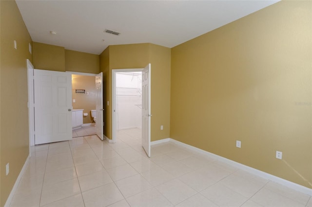 unfurnished bedroom with light tile patterned flooring, a walk in closet, connected bathroom, and a closet